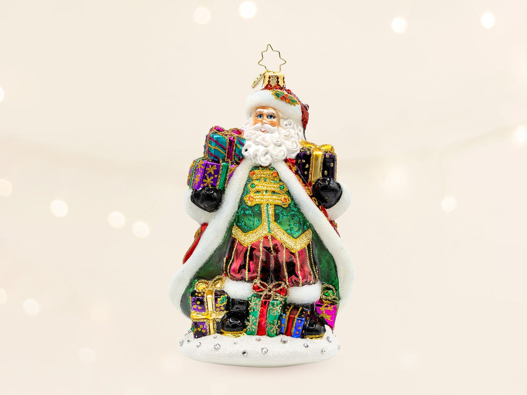 A red robed santa ornament wearing a green vest, red pants, and is holding gifts in both hands.