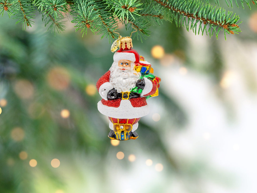 A classic red santa little gem ornament holding a bag of gifts.