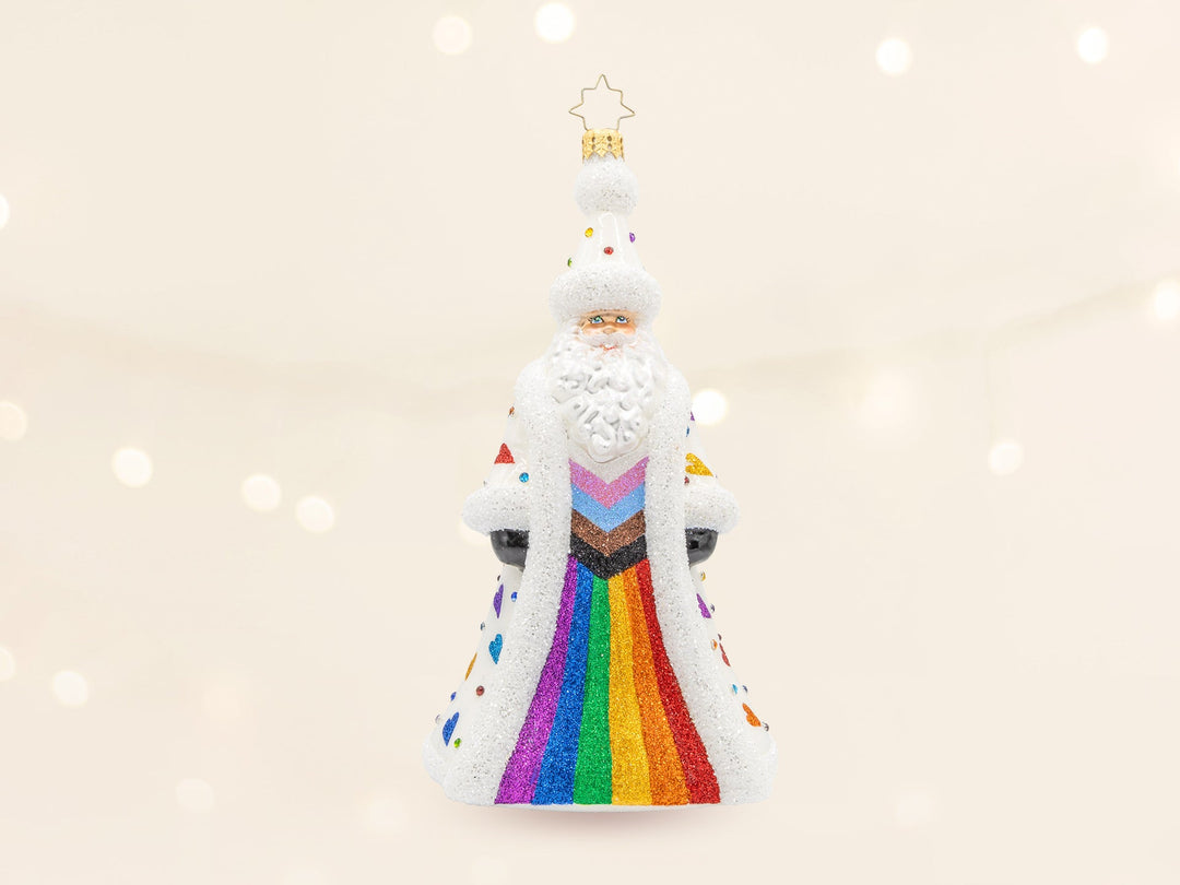 A santa ornament wearing a progress pride flag striped robe in the front and rainbow hearts on the back.