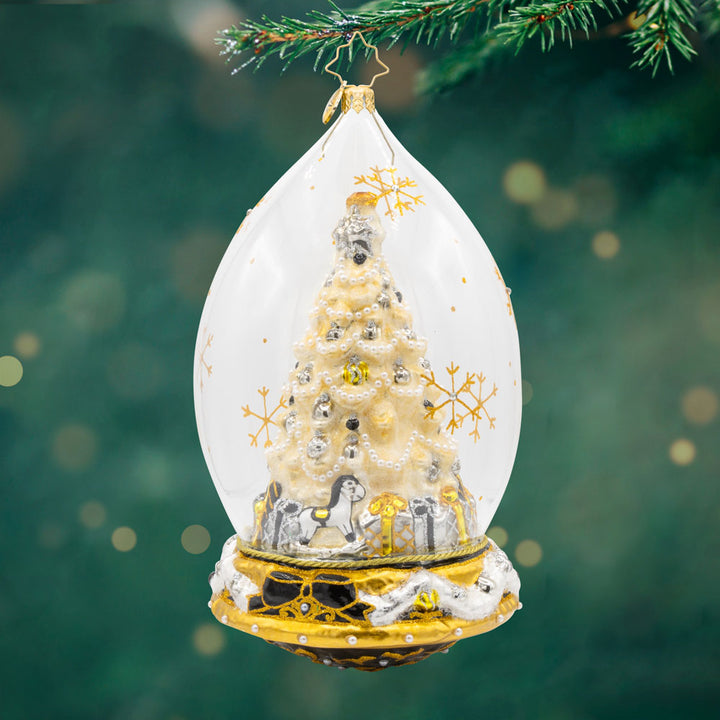 This glass dome ornament captures the essence of Christmas with a beautifully decorated tree, sparkling gifts, and a touch of festive magic. View of front.