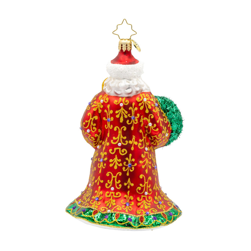 This stunning ornament showcases Santa in a resplendent red and gold robe, hand-painted with intricate designs and finished with shimmering trim. Carrying a glowing green candle and a wreath adorned with shiny holly and colorful ornaments. View of back.