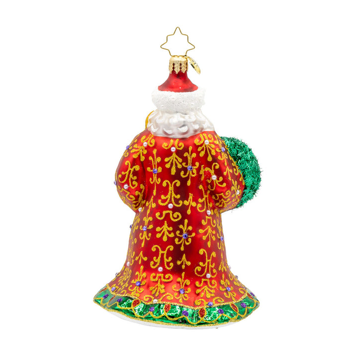 This stunning ornament showcases Santa in a resplendent red and gold robe, hand-painted with intricate designs and finished with shimmering trim. Carrying a glowing green candle and a wreath adorned with shiny holly and colorful ornaments. View of back.