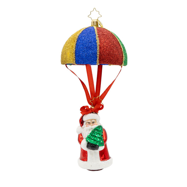 Tidings from Above Santa ornament. This ornament features Santa soaring through the air with a colorful parachute, his tiny Christmas tree in hand. View of front.