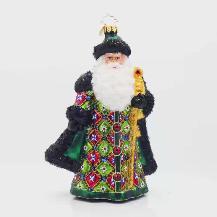 The Opulent Noel ornament. Santa is dressed in a vibrant green satin coat covered in a playful patchwork of colors and glittery designs. With his shiny gold staff, sparkling red gems, and fluffy tinsel fur trim. Video.